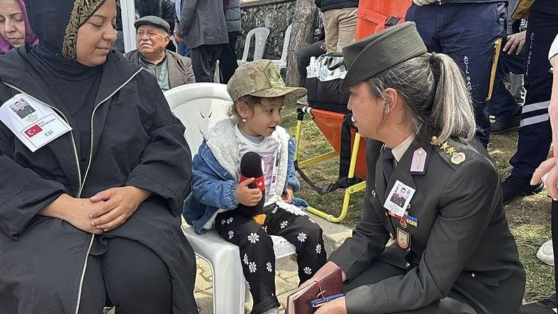 Bir kadın komutan, şehidin 4 yaşındaki kızı Alya'nın kıyafetine, babasının fotoğrafı ve ʺşehit çocuğuʺ yazan kağıdı toplu iğne ile taktı. (AA)